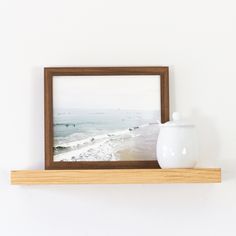 a white vase sitting on top of a wooden shelf next to a framed photo in a wood frame