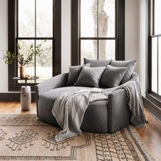 a living room with two windows and a round couch in front of the large window