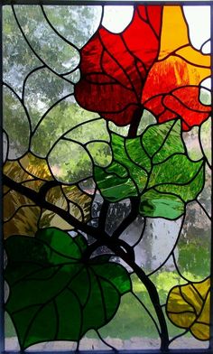 a stained glass window with flowers and leaves on it's side, in front of a tree