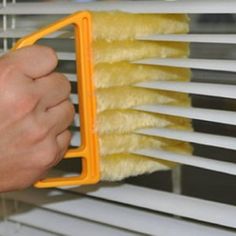 a person is cleaning the blinds with a yellow duster on it's side