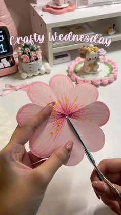 a person cutting paper flowers with scissors on a table in front of a clock and other decorations