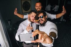 three men are taking a selfie with their cell phones in the middle of them