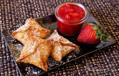 some food is sitting on a black plate with strawberries and strawberry jam in the background