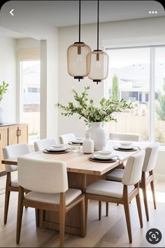 a dining room table with white chairs and a vase filled with flowers on top of it