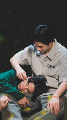 two people laying on the ground with one person touching another's head while they both have their eyes closed