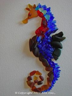 a seahorse made out of glass sitting on top of a white wall next to rocks