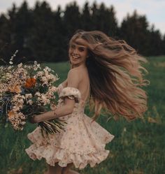 a woman in a dress is running through the grass with flowers on her head and hair blowing in the wind