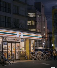 several bicycles are parked in front of a small store at night with the lights on