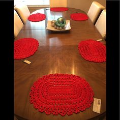 red crocheted placemats sit on a wooden table with white chairs around it