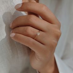 a woman's hand with a diamond ring on her left hand and a white shirt in the background