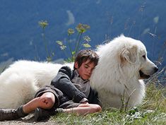 a young boy laying on the ground next to a large white dog