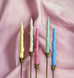 four candles are lined up in a row on a pink background with the candle holders painted different colors