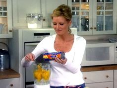 a woman standing in a kitchen holding a blender filled with food and looking at it