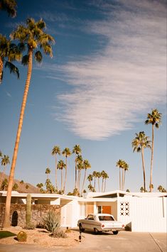 a car is parked in front of a house with palm trees on the other side