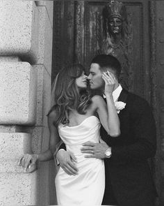 a man and woman kissing each other in front of a wall with a statue behind them