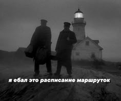 two men standing on top of a hill next to a lighthouse