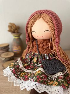 a doll with long red hair sitting on top of a wooden table next to a vase