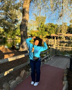 a woman standing on a walkway with her hands behind her head and trees in the background