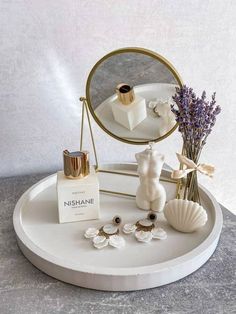 a white tray topped with a mirror and some jewelry next to a vase filled with flowers