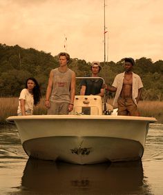 four people standing on the back of a boat in water with trees in the background