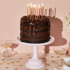 a chocolate cake sitting on top of a table with wine glasses and flowers in front of it