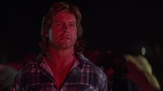 a man standing in the dark with his eyes wide open and looking at something while wearing a flannel shirt