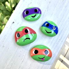 four painted turtles sitting on top of a white wooden table next to green plants and bushes