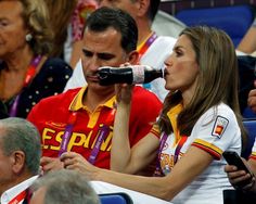 a woman drinking from a bottle while sitting next to a man in a red shirt