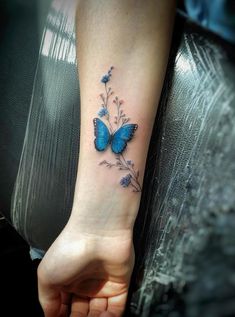 a small blue butterfly tattoo on the left inner arm and wrist, with flowers around it