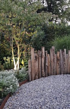 a wooden fence is surrounded by gravel and plants in the background, along with some trees