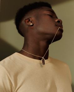 a young man with his eyes closed wearing a gold necklace and earring, standing in front of a white wall