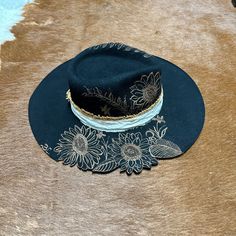 Rancher style cowboy hat for cowgirls custom burned by hand exclusively for Bourbon Cowgirl! We worked with this popular designer to create our very own look. 100% wool rancher hat in black which looks great with every outfit. One size fits all, as the interior band is adjustable to fit most. A beautiful rancher style with a pinch crease, this gorgeous black cowgirl hat is sanded and torched to a beautifully burnished and distressed finish. Firm shape (do not crush). Our artisan has hand burned a beautiful galloping horse with flowing mane up the side of the crown with sunflowers and wildflowers trailing around the brim. The words Sunflowers are the centerpiece of this rancher style flat brimmed custom burned hat by KC Lids. Cut with a live edge, this is a showstopper! The 100% silk hat ba Custom Burned Hats, Burn Hats Ideas, Wood Burn Hat, Painted Hats For Women, Felt Hat Burning Designs, Hat Burning Ideas, Diy Leather Hat, Hat Burning Designs, Sunflowers And Wildflowers