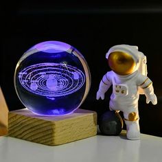 an astronaut figurine next to a crystal ball on a wooden stand with a blue light