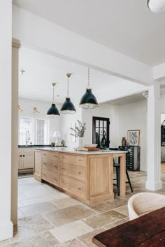 an open kitchen and living room area with white walls, beige flooring and black pendant lights