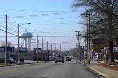 cars are driving down the street in front of buildings and water towers on poles with power lines above them