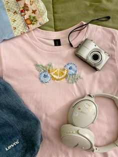 a t - shirt, headphones and a camera on a bed