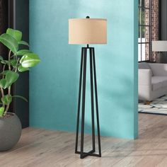 the floor lamp is next to a potted plant in front of a blue wall