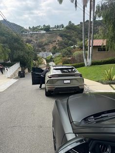 two cars parked on the side of a road next to a house and palm trees