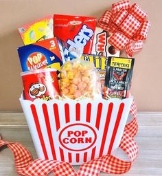 a popcorn box filled with snacks and candy on top of a wooden table next to a red ribbon