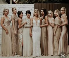 a group of women standing next to each other in long dresses on a sidewalk near a brick wall