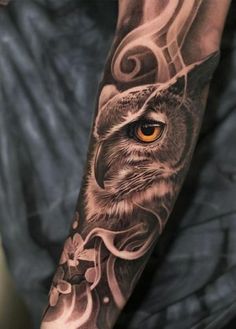 an owl tattoo on the arm with flowers and swirls around it's eyes