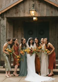 a group of women standing next to each other in front of a wooden building holding bouquets