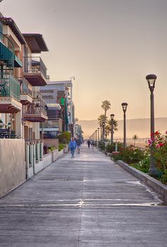 two people walking down an empty street in front of some apartment buildings and palm trees