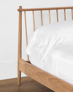 a wooden bed frame with white sheets and pillows on top of it, in front of a white wall