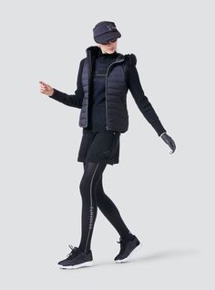 a woman in black is walking with her hands out to the side, wearing a hoodie and leggings