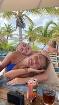 two beautiful women laying on top of a wooden table next to each other near some drinks