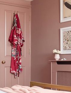 a bedroom with pink walls and clothes hanging on the door handle, next to a bed