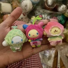 someone is holding three small keychains in their hand, one has a pink and green doll on it