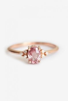 a pink diamond ring with three diamonds around it on a white surface, in front of a plain background