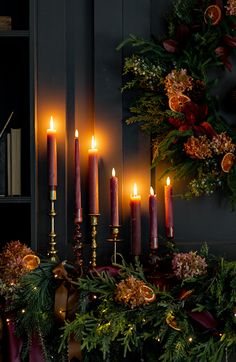 candles are lit in front of a christmas wreath